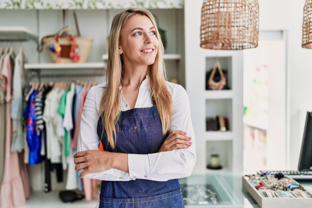 Female business owner wearing a denium apron looking up with a smile on her face and crossed arms
